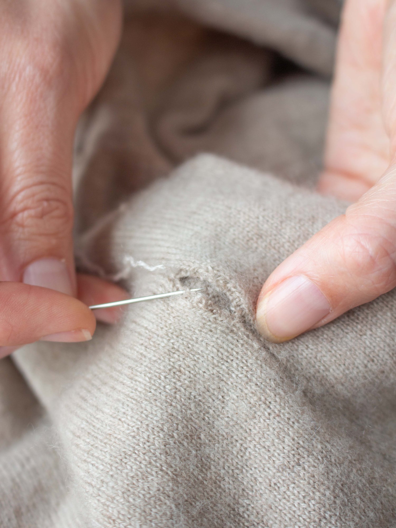 Person sewing a small hole in cashmere fabric with a needle.