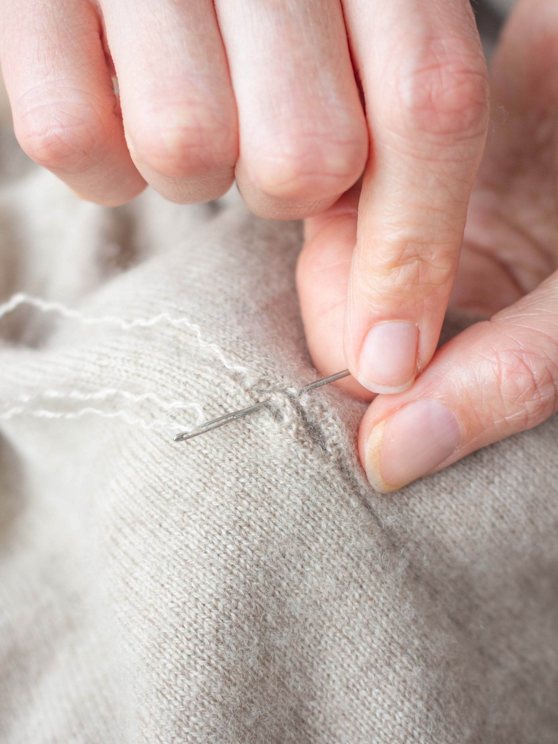 Close-up of hands mending a cashmere jumper.