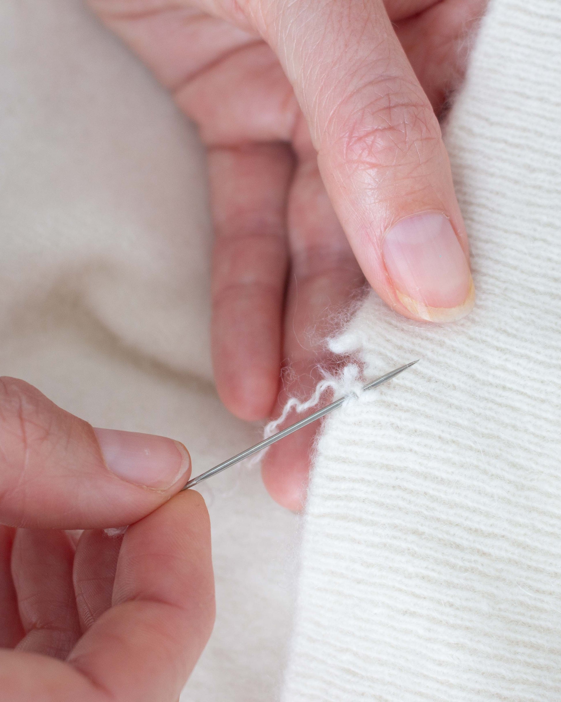 Hands mending a white cashmere jumper
