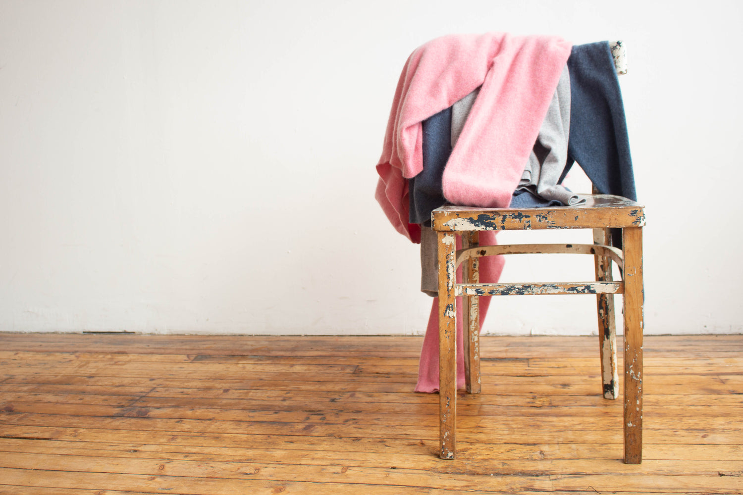 Stack of secondhand cashmere clothes on a wooden stool against a white wall