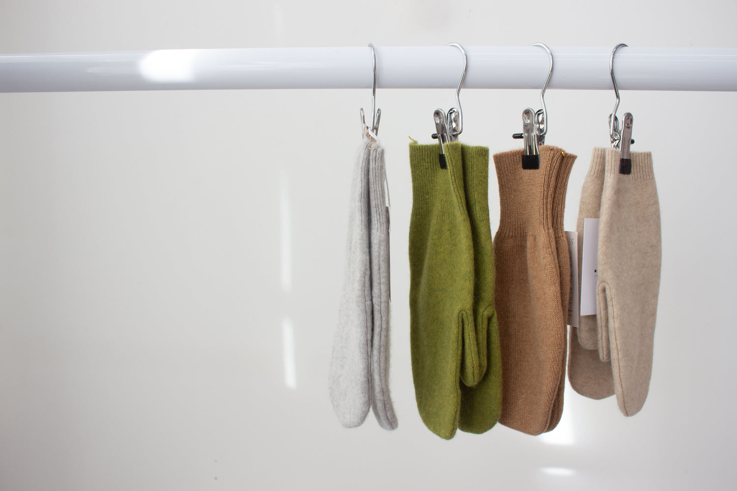 Four cashmere mittens hanging on a rack against a white background