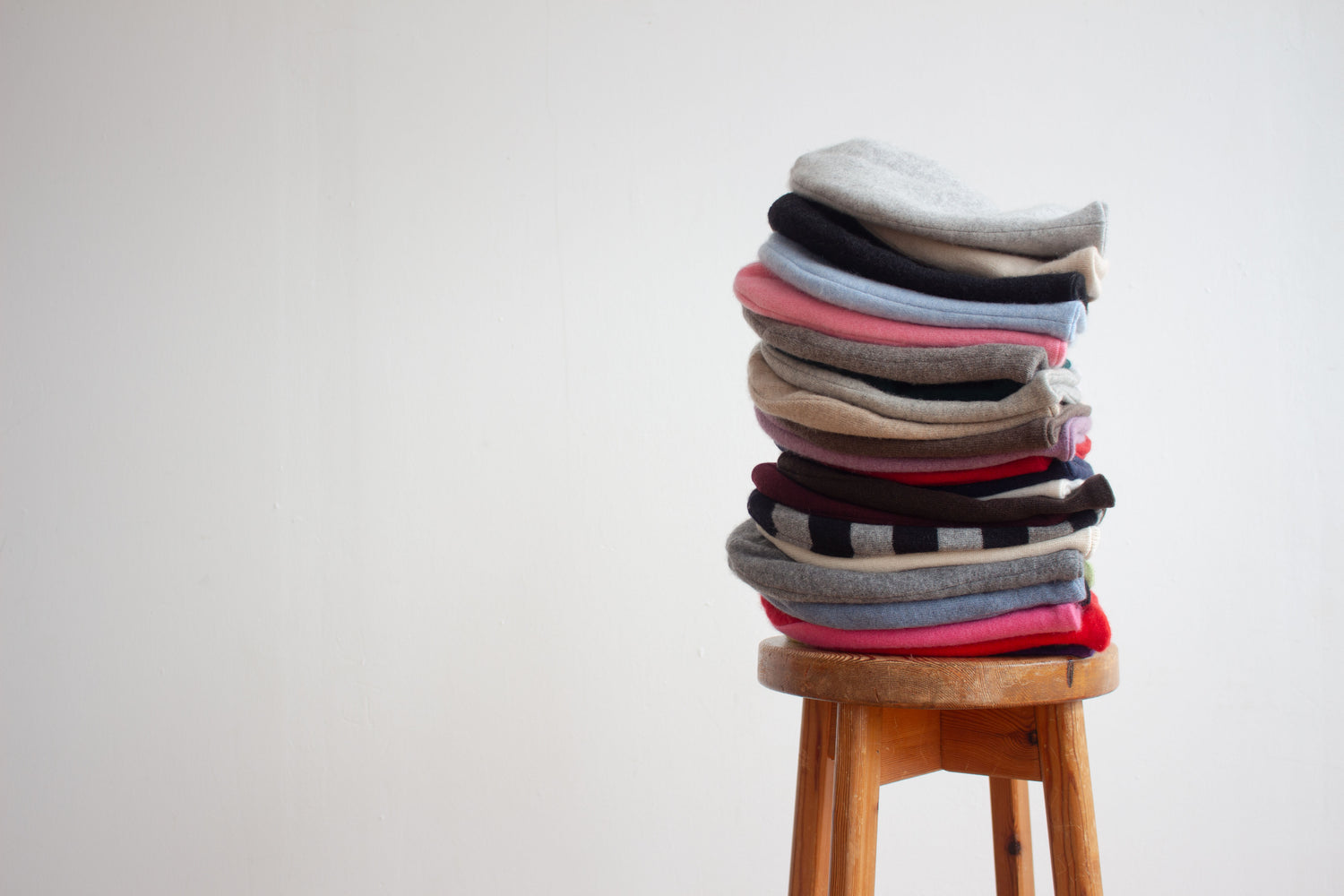 Stack of colourful cashmere beanies on a wooden stool with a plain background