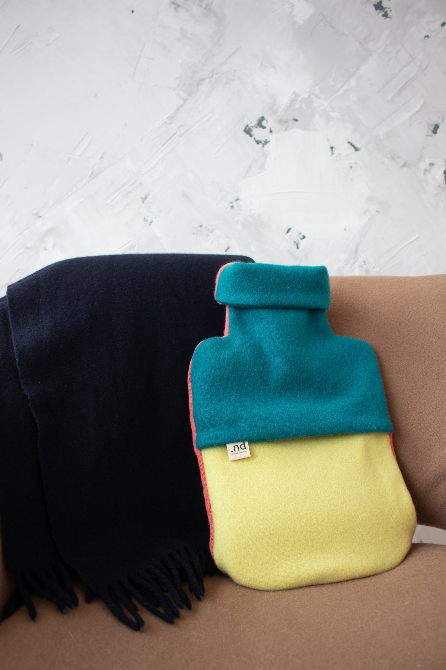 Cashmere hot water bottle with blue cover and yellow base on a textured surface.