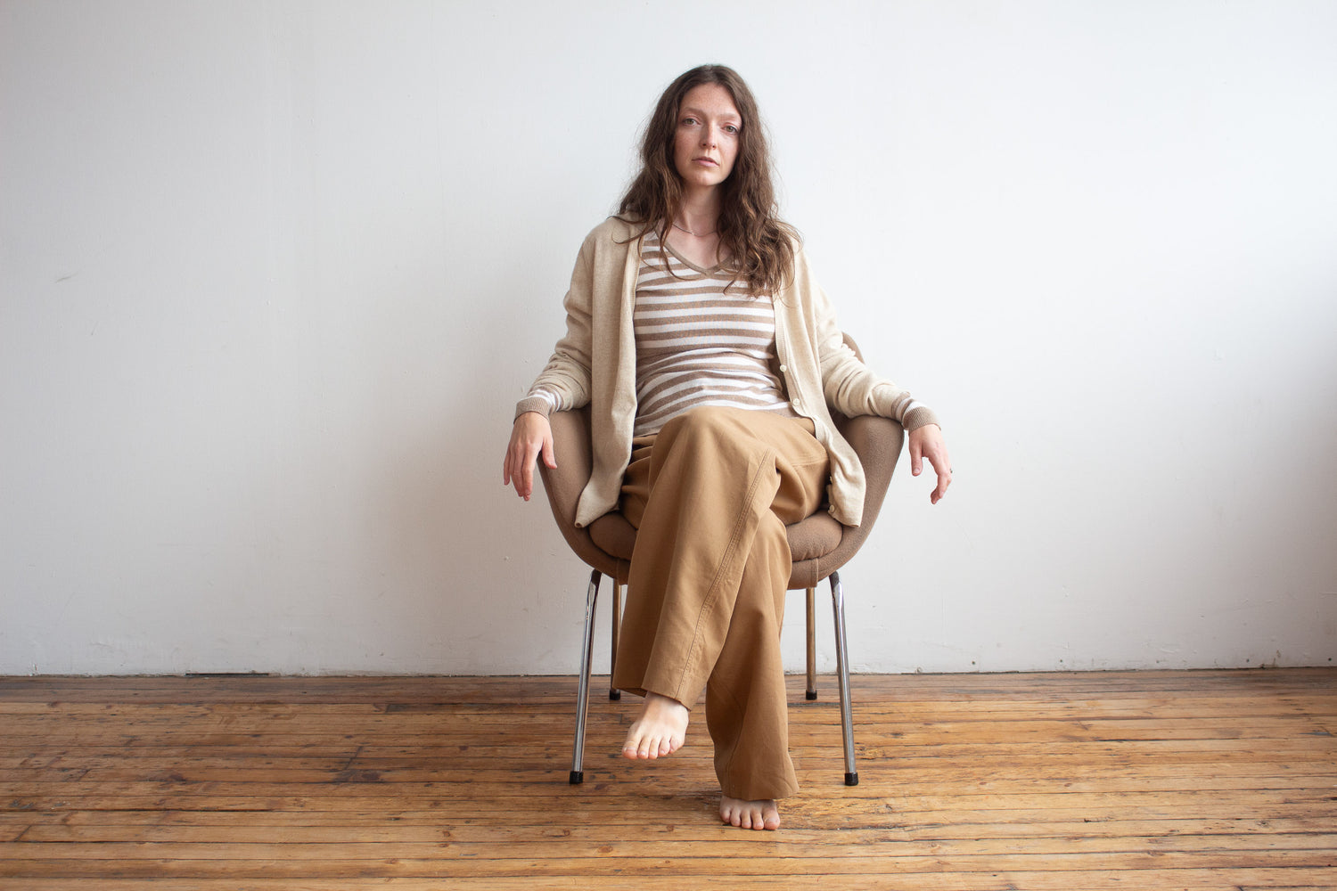 Woman sitting on a chair in a minimalistic room with wooden floor and white walls.