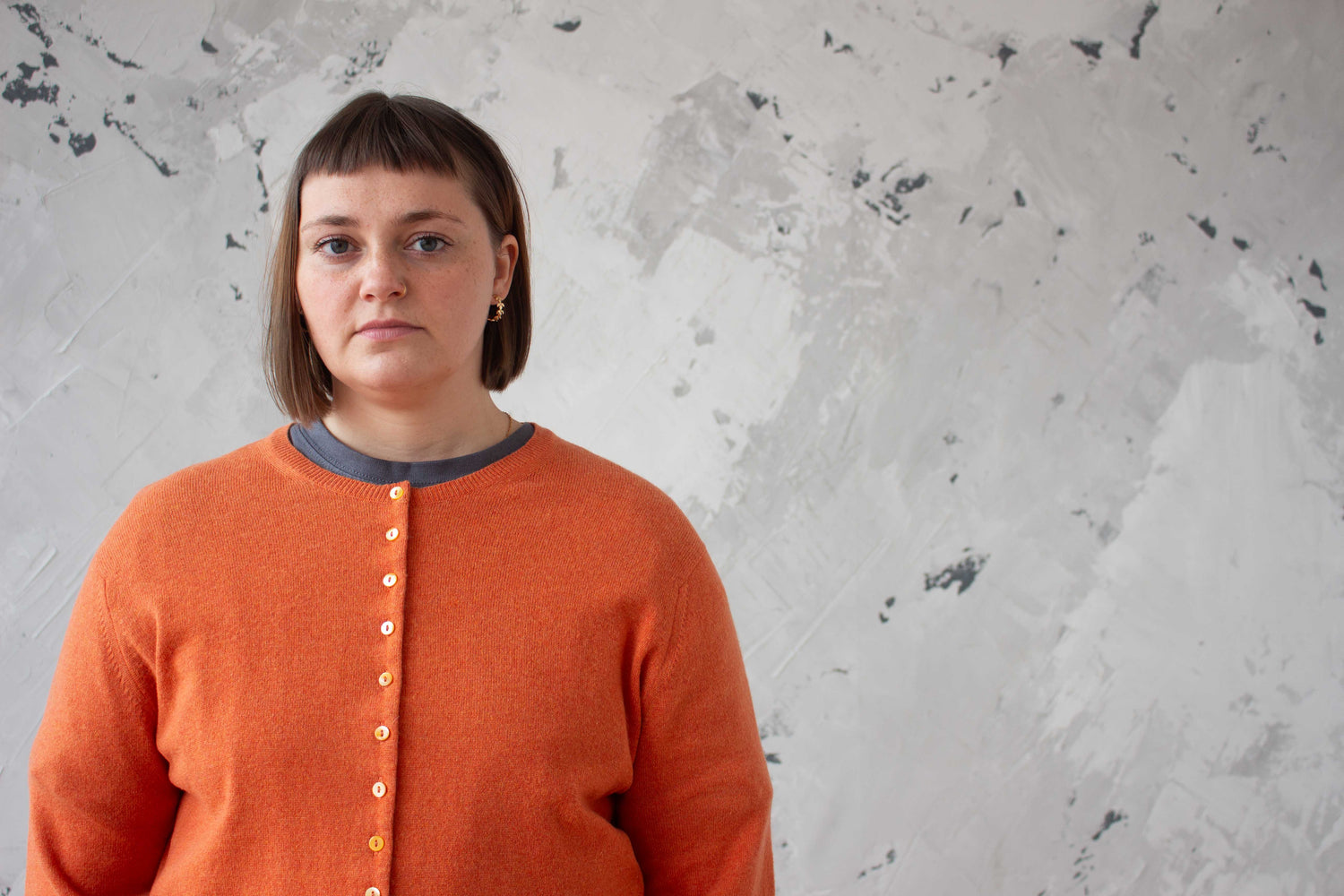 Person wearing an orange cashmere sweater against a textured grey wall